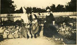 Three women in costume sat on a wall