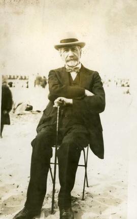 Unidentified man on a chair on sand with cane