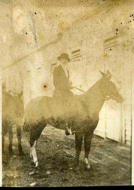 Unidentified woman on a horse by an unidentified building