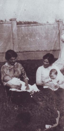 two women sat on grass outside of walled garden holding their babies