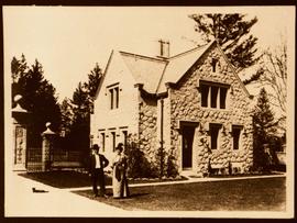 Sooke Road gatehouse with two people in driveway, and a cat. Possibly Herman and Theresa Eng