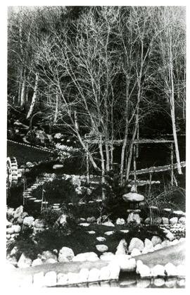 Stone lined paths in Japanese garden in winter, waterwheel on left