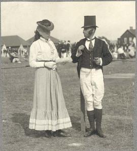 man and woman on a field, possibly a hunting or riding gathering, possibly in costume