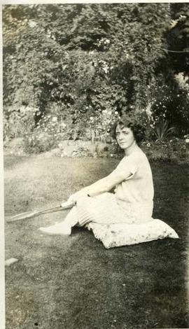 Muriel with a badminton racket, sat on cushion on lawn