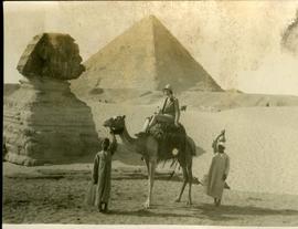 Woman on camel at Cheops pyramids with Sphinx, two men standing